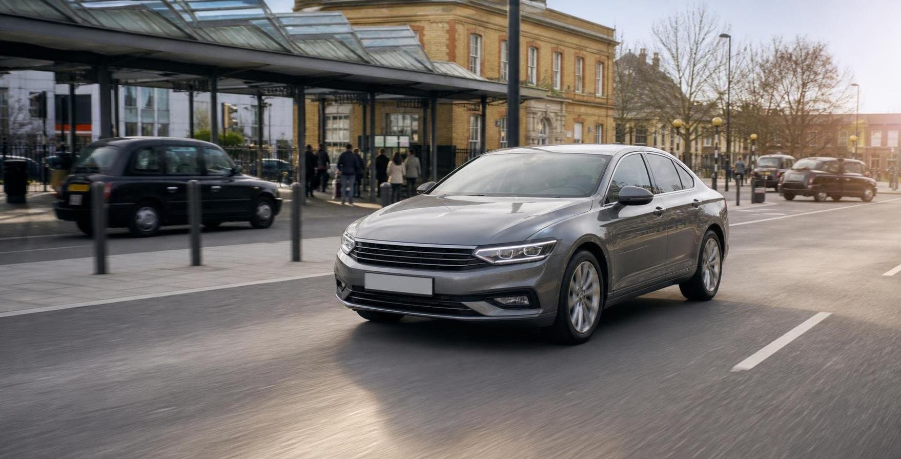 Mid-size hire car driving past a station approach road in a London suburban setting